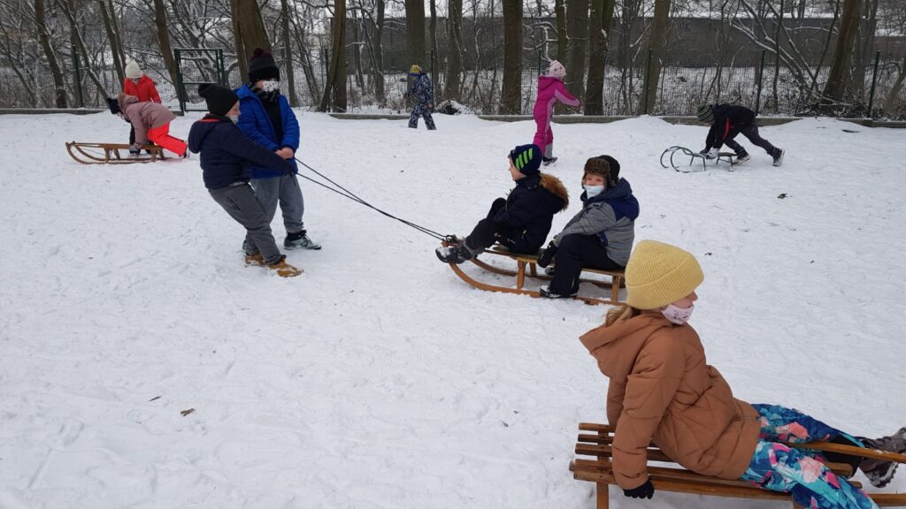 Zabawy na śniegu: sanna a w oddali rzuty śnieżkami.